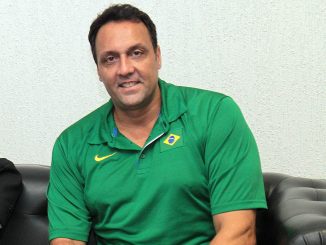 Pampa, ex-jogador de vôlei, vestido com polo verde da seleção brasileira, sentado e sorrindo.