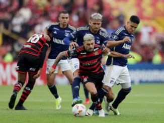 Foto mostra cinco jogadores, três do Millonarios Fútbol Club e dois do Clube de Regatas Flamengo com seus respectivos uniformes, em jogo válido pela Copa Libertadores da América, em Bogotá