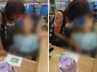 Mulher tenta ajustar a cabeça de um corpo sentado em uma cadeira de rodas diante do balcão de banco em Bangu.